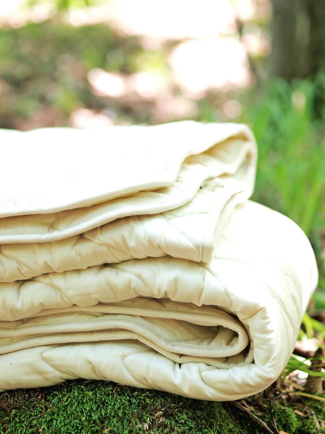Folded cotton sateen and wool padding duvet insert on a grassy ground with a blurred natural background. Handmade by Woolland
