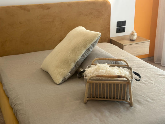 Bed with natural linen and merino wool pillows and wooden basket with raw on a bed in a bedroom setting by the Woolland