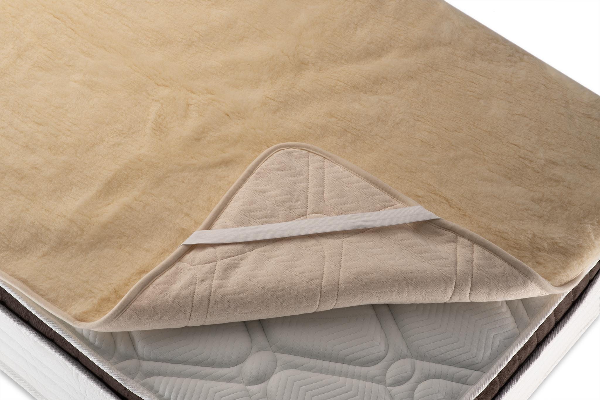 Merino wool quilted mattress cover with elastic bands on a bed with a white background. Handcrafted by Woolland