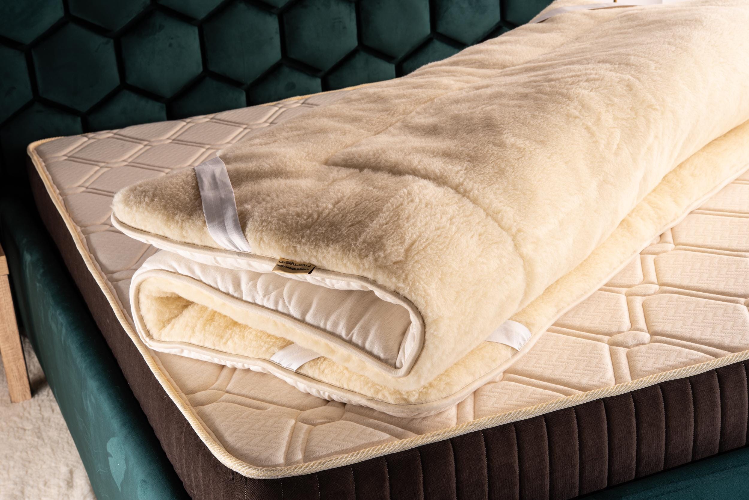 Folded merino mattress topper on a bed with a green hexagonal patterned headboard. Handcrafted by Woolland