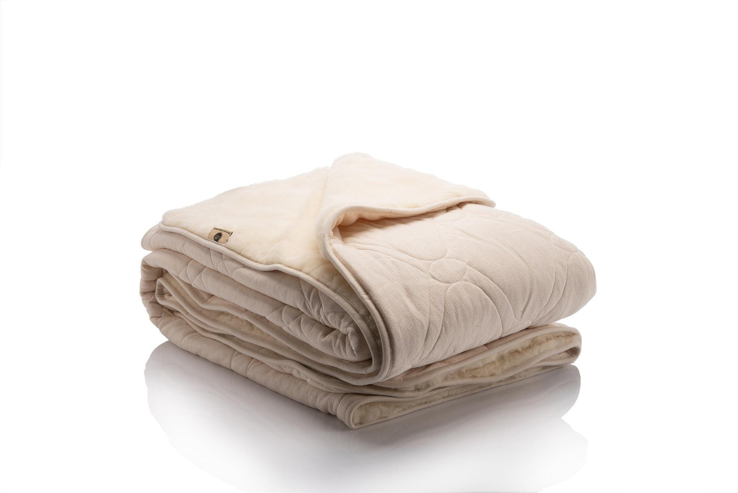 Reversible blanket with one side in soft cream organic cotton quilted with wool padding and the other side in natural beige merino wool, shown folded to highlight both textures. Made by Woolland