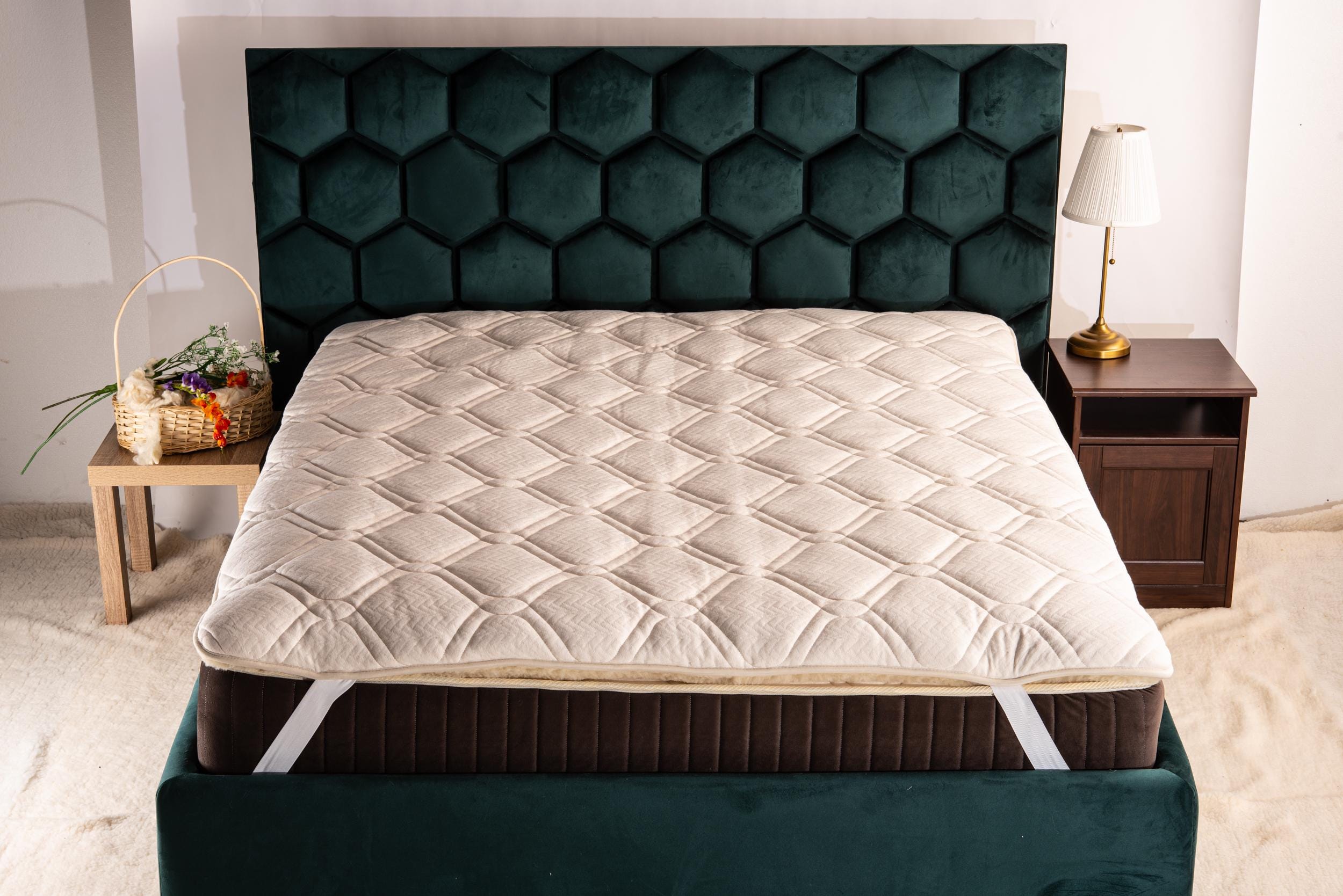 Mattress topper with linen on a bed with a green headboard in a bedroom setting by the Woolland eu