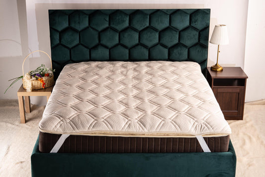 Mattress topper with linen on a bed with a green headboard in a bedroom setting by the Woolland eu