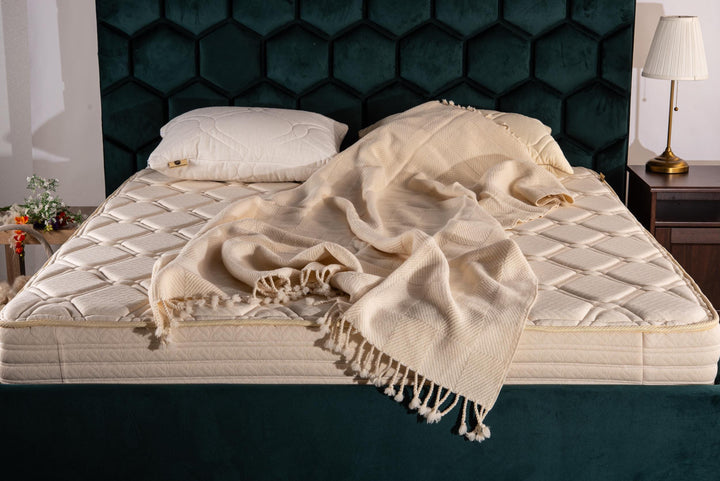 Finest soft merino wool throw blanket draped over a mattress with a dark green hexagonal patterned headboard. Handmade by Woolland
