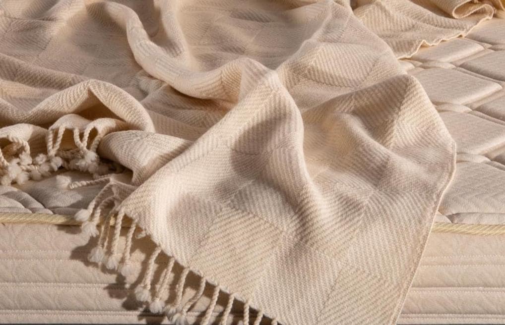 Closeup of woven merino wool blanket with fringes on a textured surface. Handcrafted by the Woolland