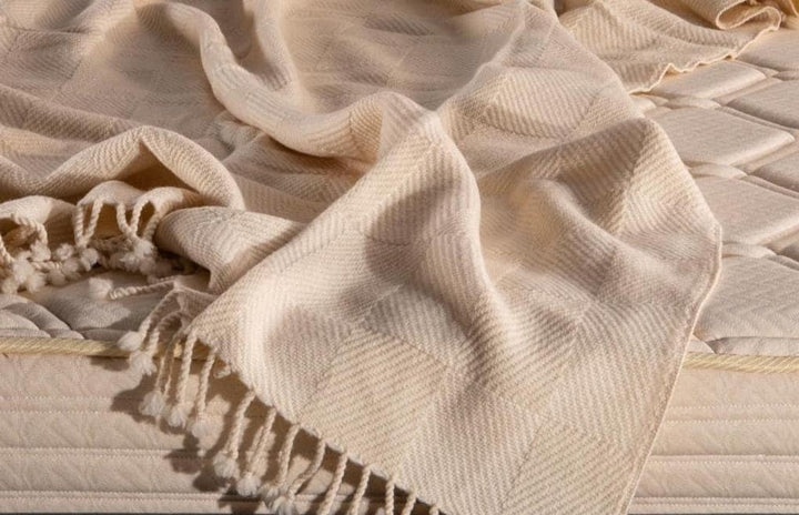 Closeup of woven merino wool blanket with fringes on a textured surface. Handcrafted by the Woolland
