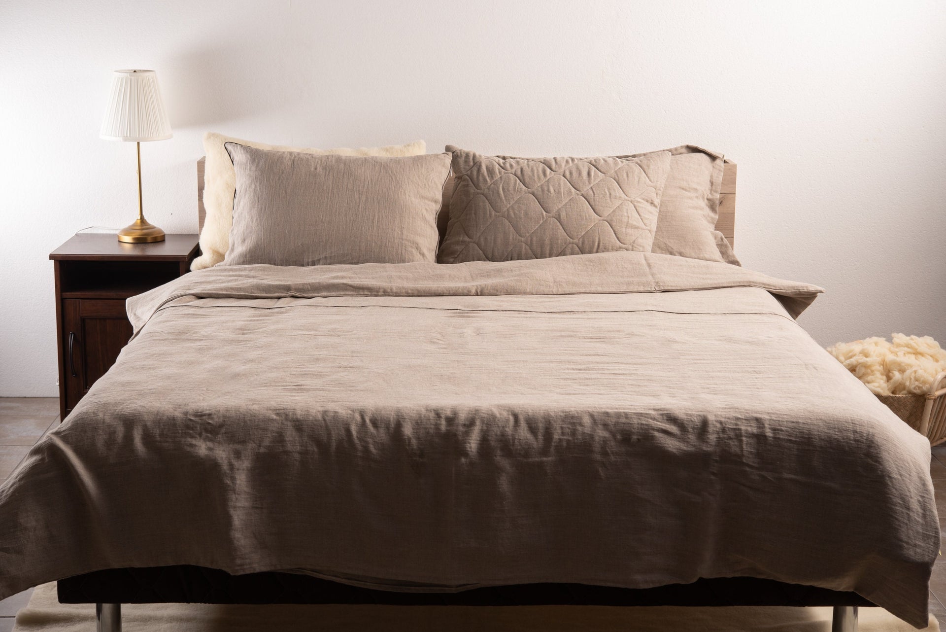 Pure linen bedding set on a bed with a lamp and basket in the background by the Woolland