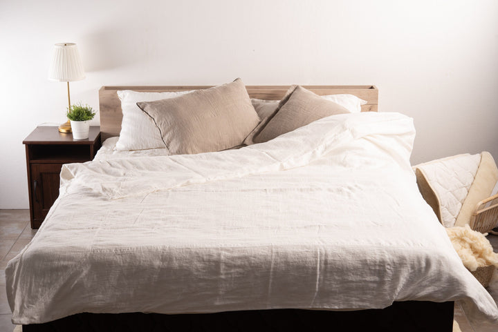 Neatly made bed with white linen bedding and pillows in a bedroom. Handcrafted by the Woolland.