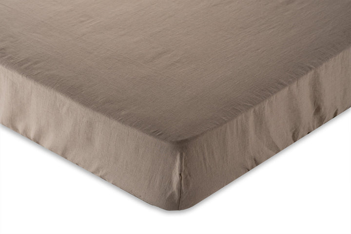 Natural linen fitted sheet on a mattress with a plain background. Hand made by Woolland