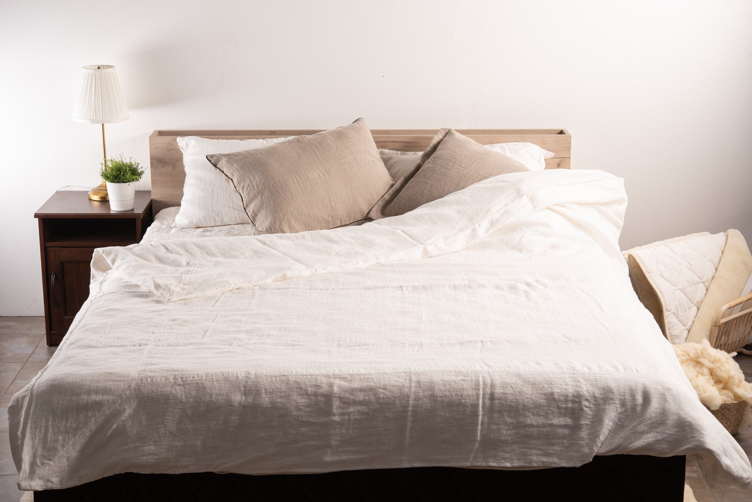 Neatly made bed with white linen bedding and pillows in a bedroom setting.