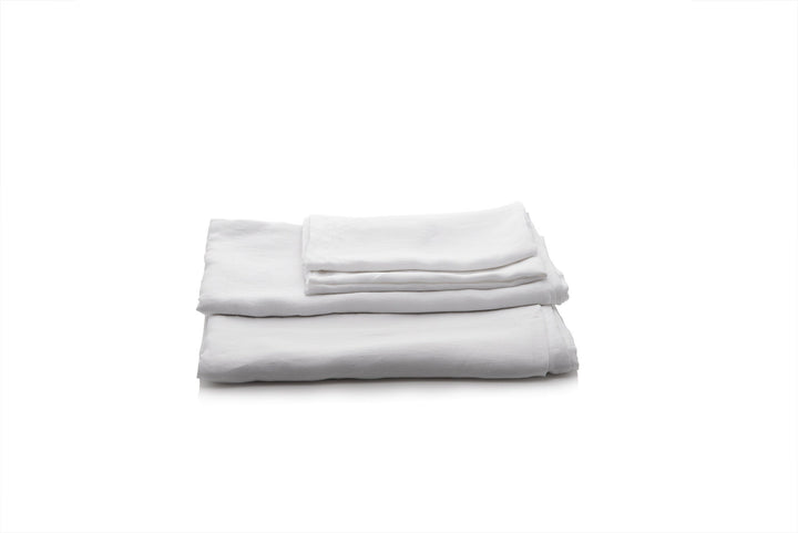 Folded white linen bed sheets on a white background by Woolland