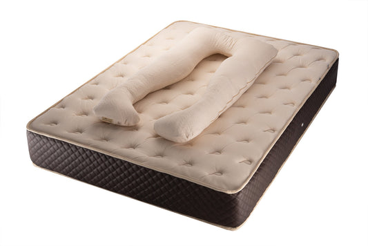 A beige organic cotton cover and wool stuffed U-shaped pregnancy pillow on a brown mattress, showcasing its form and intended use for full body support during pregnancy. By the Woolland 