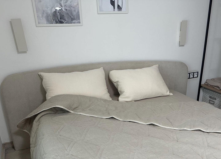 Bed with beige bedding and organic cotton pillows in a room with framed pictures on the wall handmade by woolland.