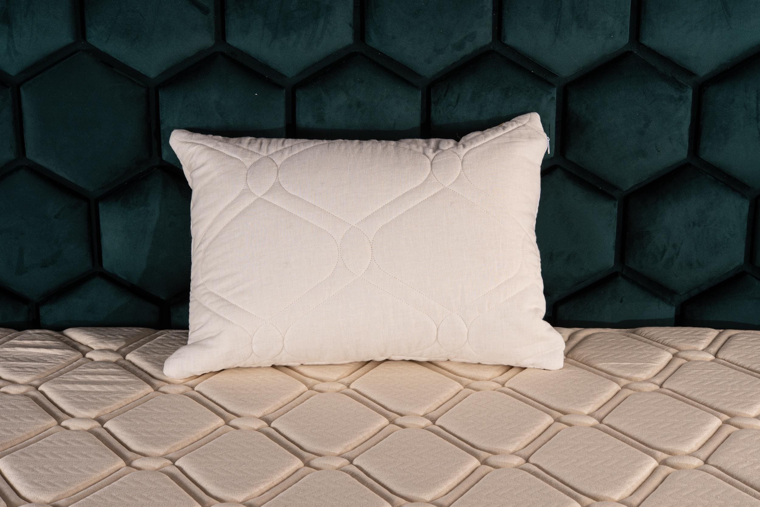 White linen cover and kapok filled pillow on a textured surface with a dark hexagonal patterned wall in the background by Woolland