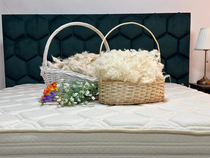 Two wicker baskets filled with raw kaok and raw wool fluffy materials on a mattress with a decorative headboard.