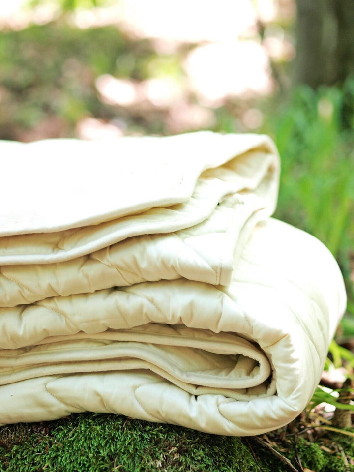 Folded cotton sateen and wool padding duvet insert on a grassy ground with a blurred natural background. Handmade by Woolland