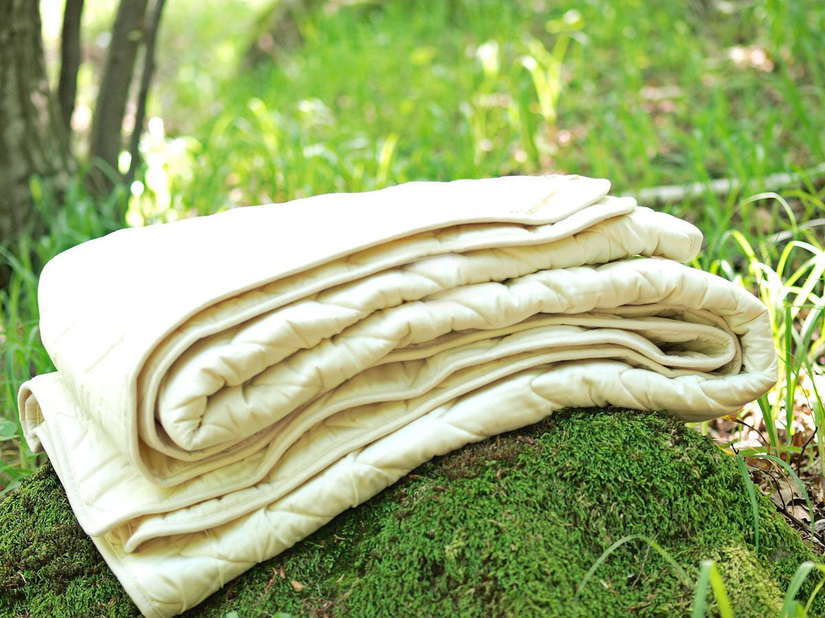 Folded cotton sateen and wool filling blanket on a mossy rock in a forest setting. Handmade by Woolland.