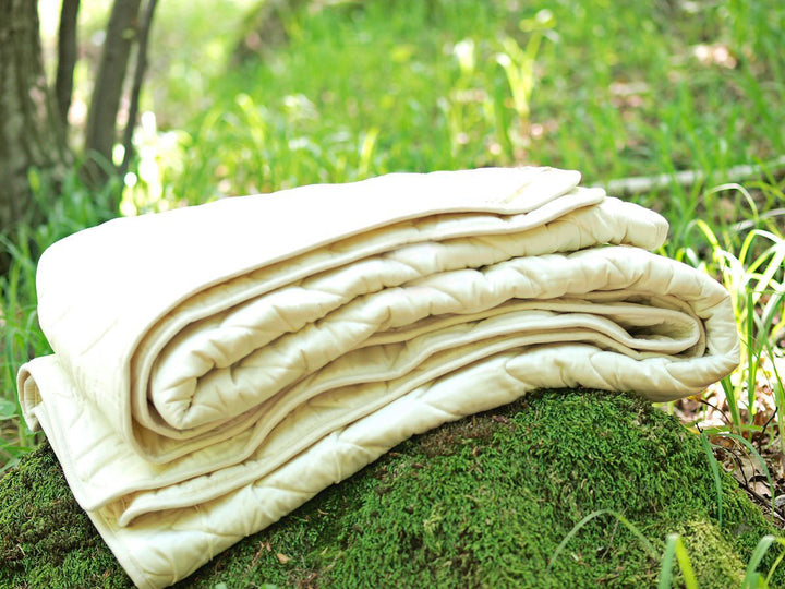 Folded cotton sateen and wool filling blanket on a mossy rock in a forest setting. Handmade by Woolland.