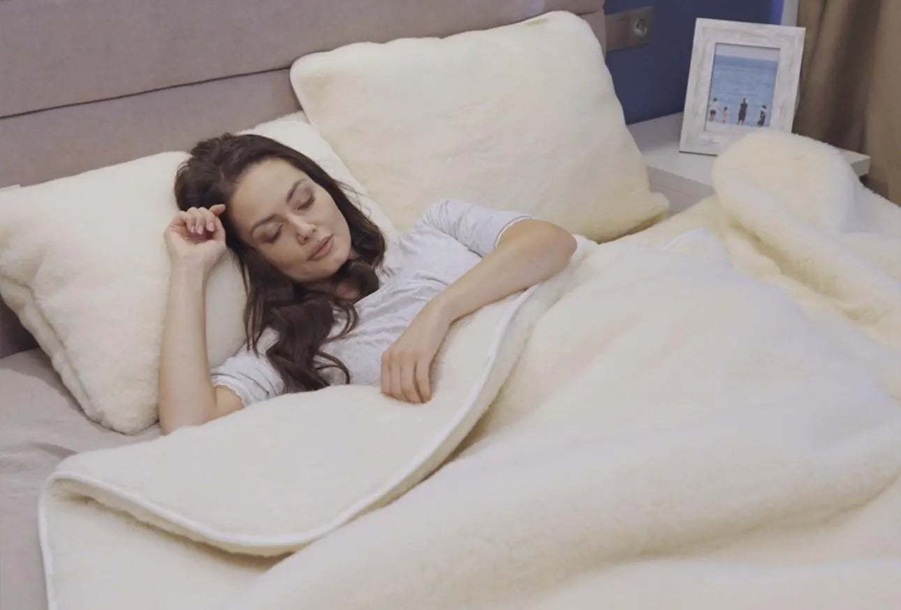 Woman sleeping under a merino wool comforter on a bed with pillows. Handmade by Woolland