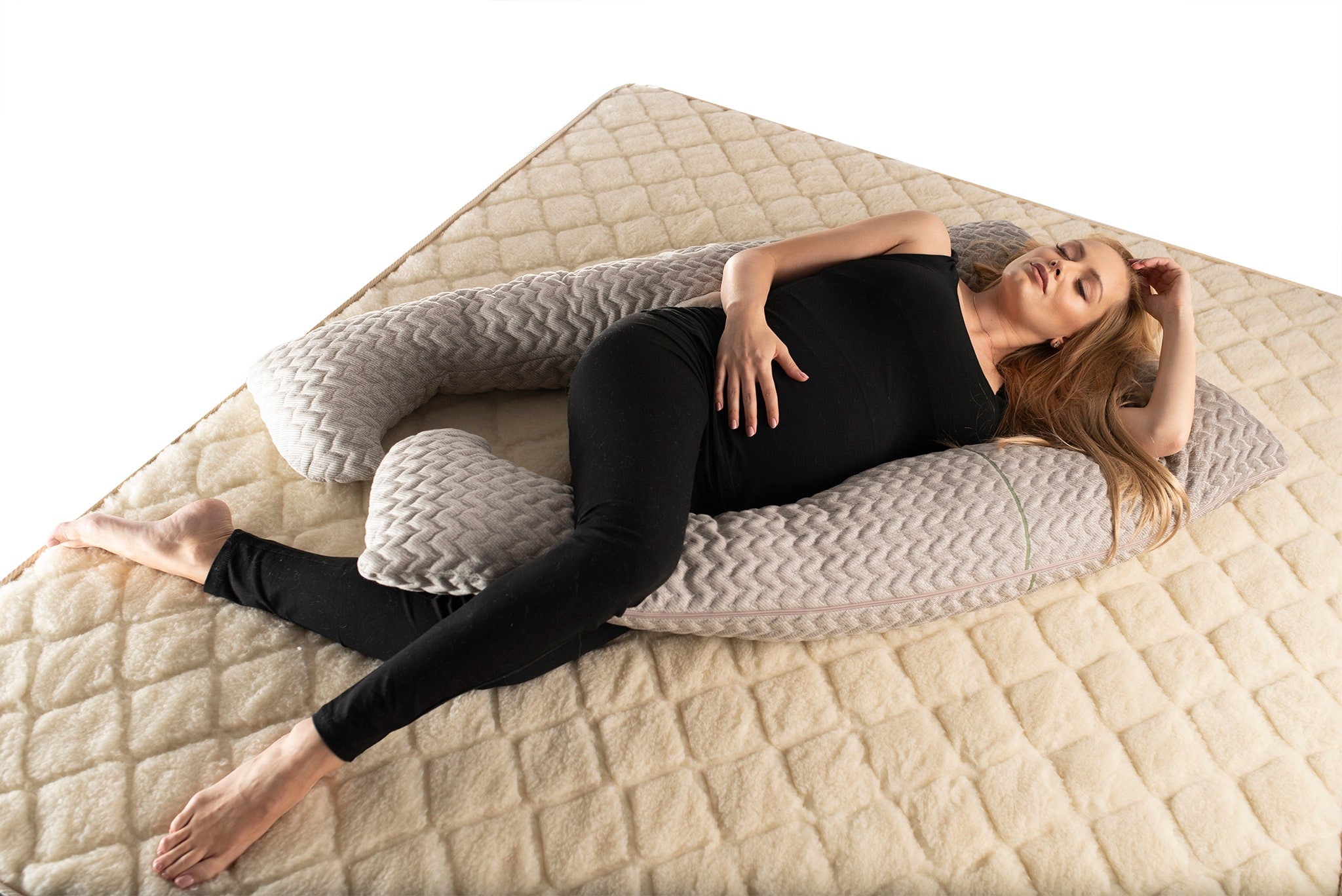 A pregnant woman lying comfortably on her side on U-shaped pregnancy pillow with a zipper case made by the Woolland 