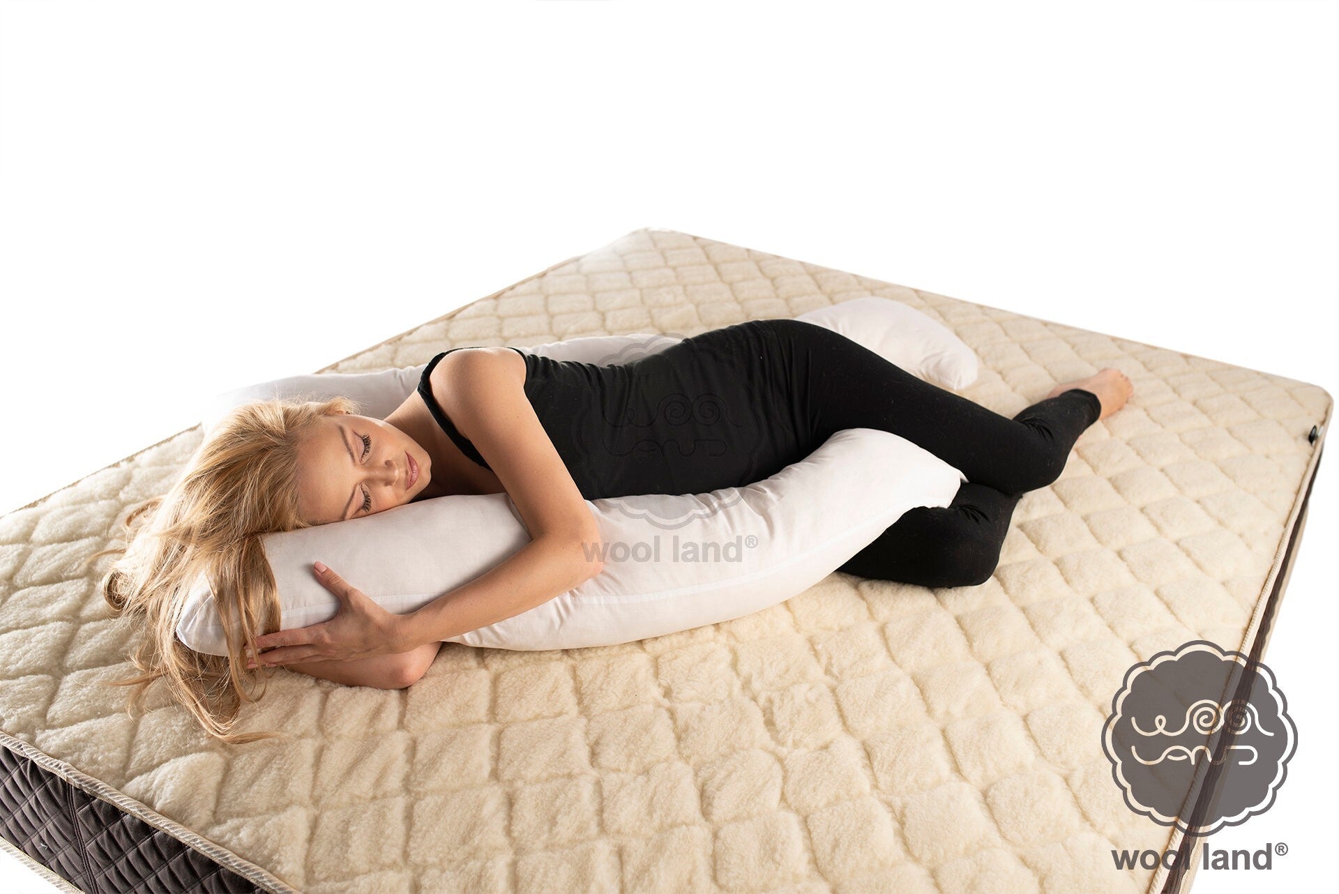 A pregnant woman is laying on a bed snuggling a white organic fibers u-shaped pregnancy pillow handmade by Woolland