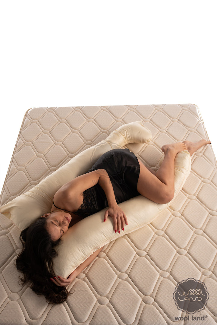 A pregnant lady is laying on a bed snuggling a organic fibers u-shaped pregnancy pillow handcrafted by Woolland