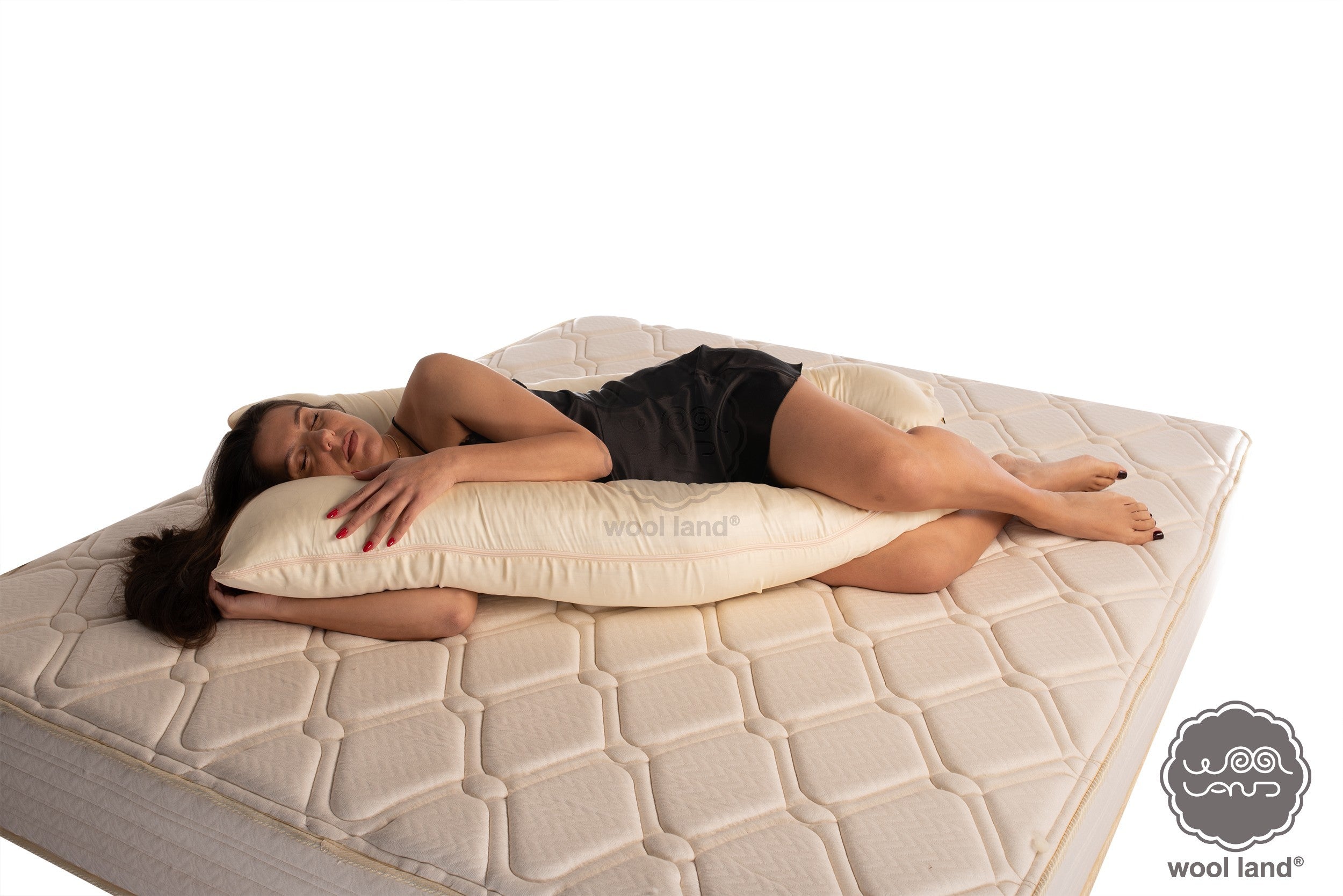 A frontal look of beautiful pregnant lady is laying on a bed snuggling a organic fibers u-shaped pregnancy pillow handcrafted by Woolland