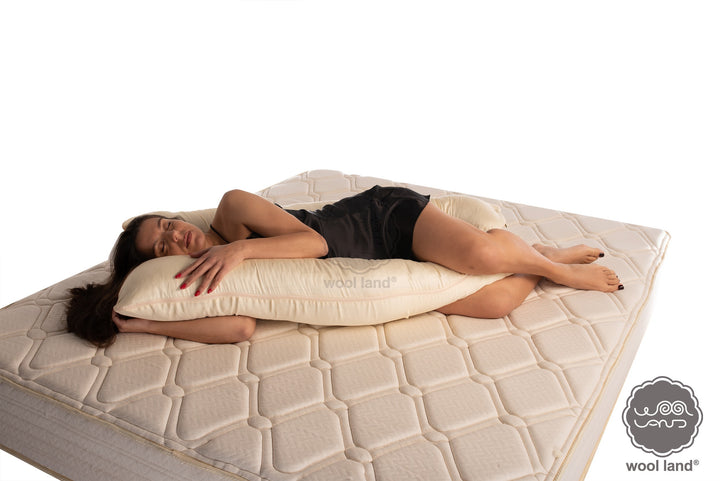 A frontal look of beautiful pregnant lady is laying on a bed snuggling a organic fibers u-shaped pregnancy pillow handcrafted by Woolland