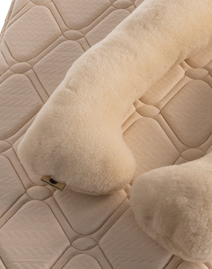 The Woolland merino wool pregnancy pillow on a quilted surface 