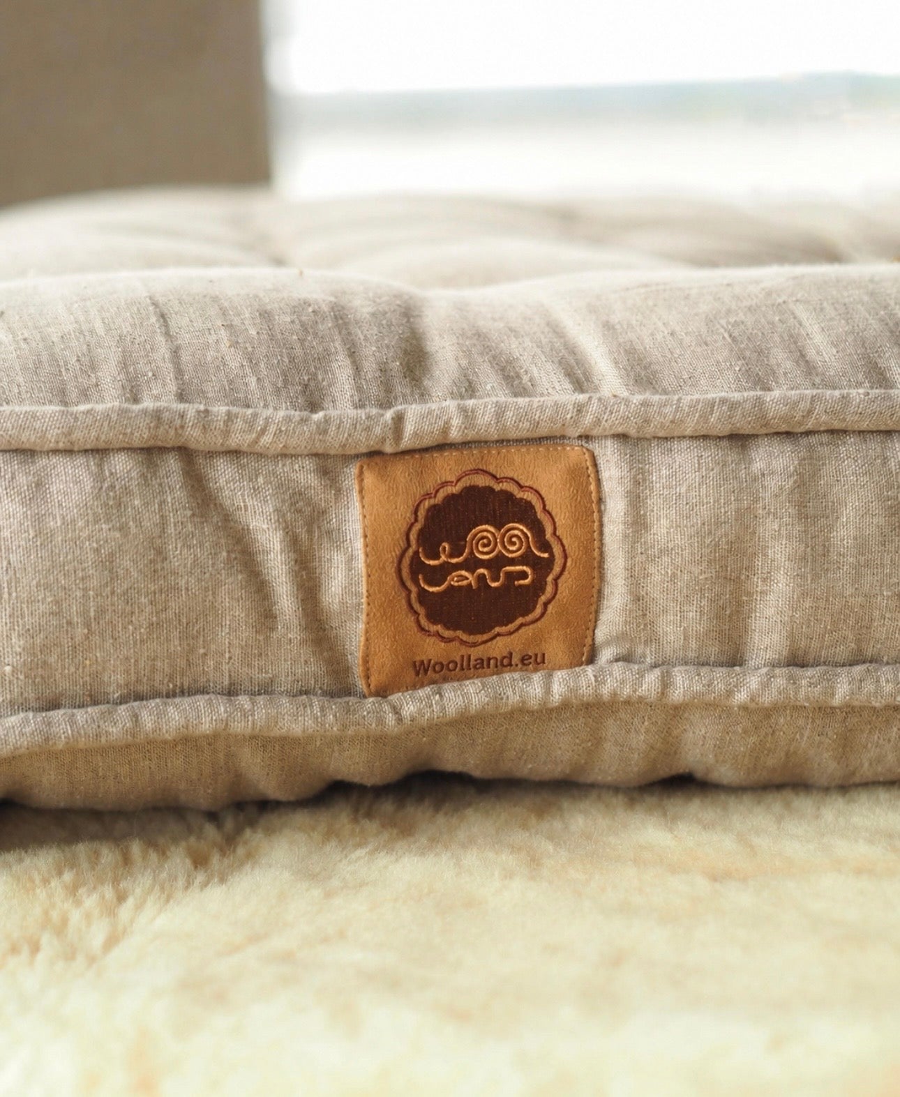 Beige handmade Woolland linen and wool mattress with a visible brand label on a floor. background