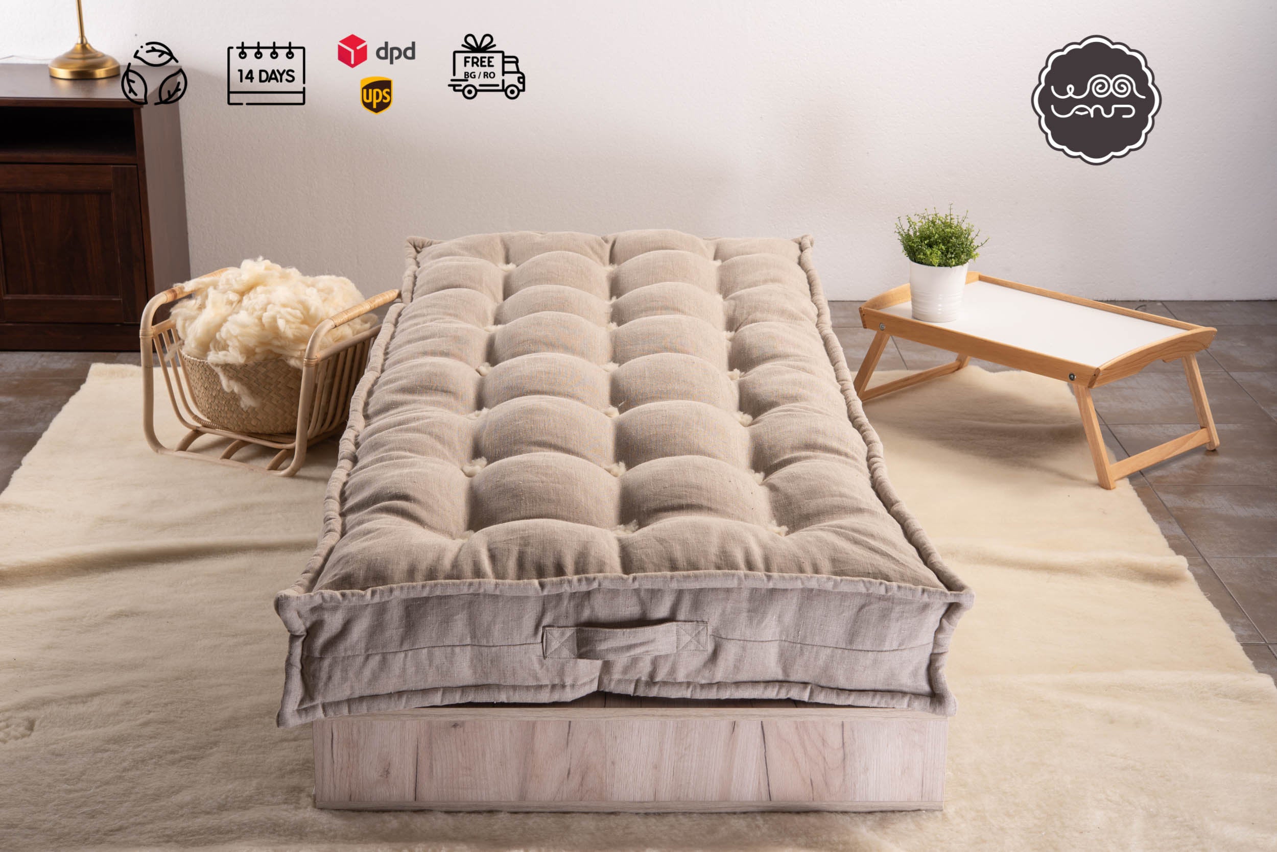 A mattress topped with merino wool and linen, displayed on a bed frame with a linen cover, set against a neutral background with a wicker chair and a small wooden side table in the background.