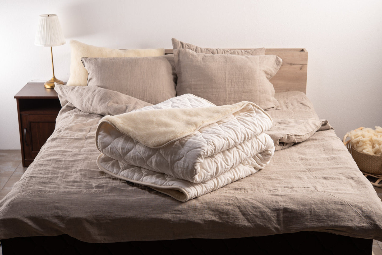 Folded white linen and merino wool reversible blanket on a bed with linen pillows and linen bedding set