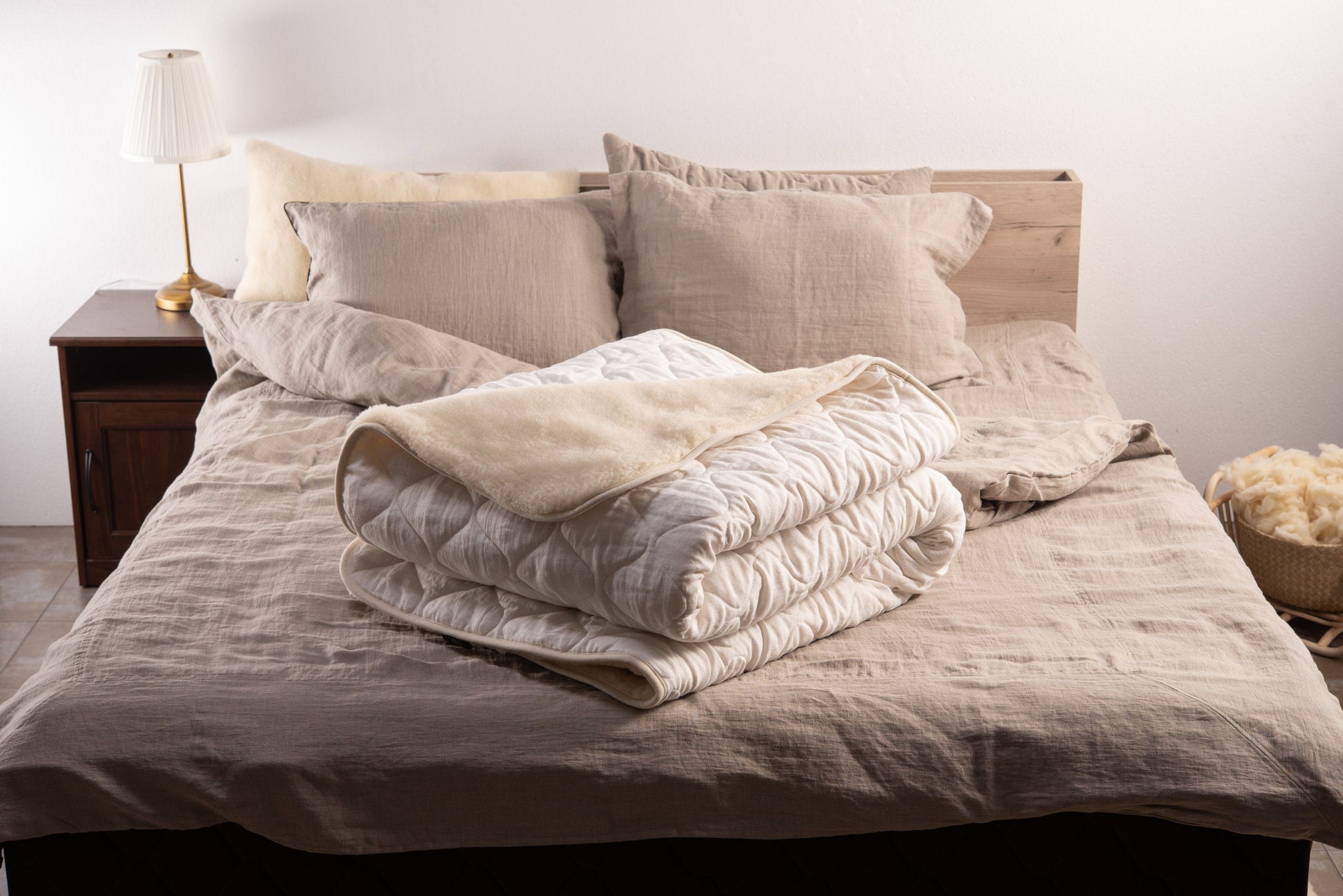 Folded white linen and merino wool reversible blanket on a bed with linen pillows and linen bedding set