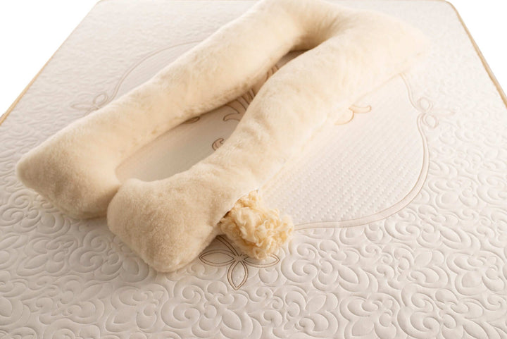 A beige, u-shaped full body merino wool pillow on a bed, designed for pregnancy support. Handmade by the Woolland